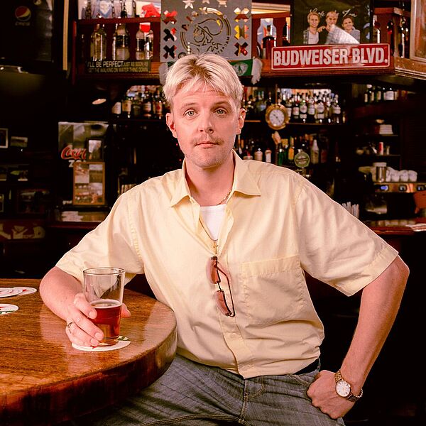 Campagnefoto van Jim Deddes, zittend aan een tafel in een café met een glas bier in zijn hand