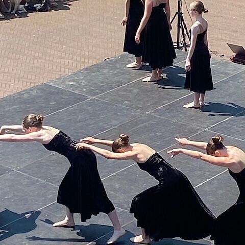 vrouwen in zwarte jurken dansen op een podium in de buitenlucht