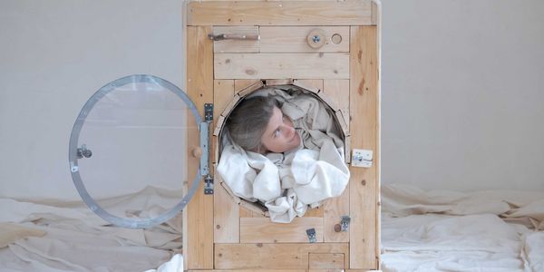 Een foto van Dieske Krijnders die met haar hoofd uit een houten wasmachine kijkt