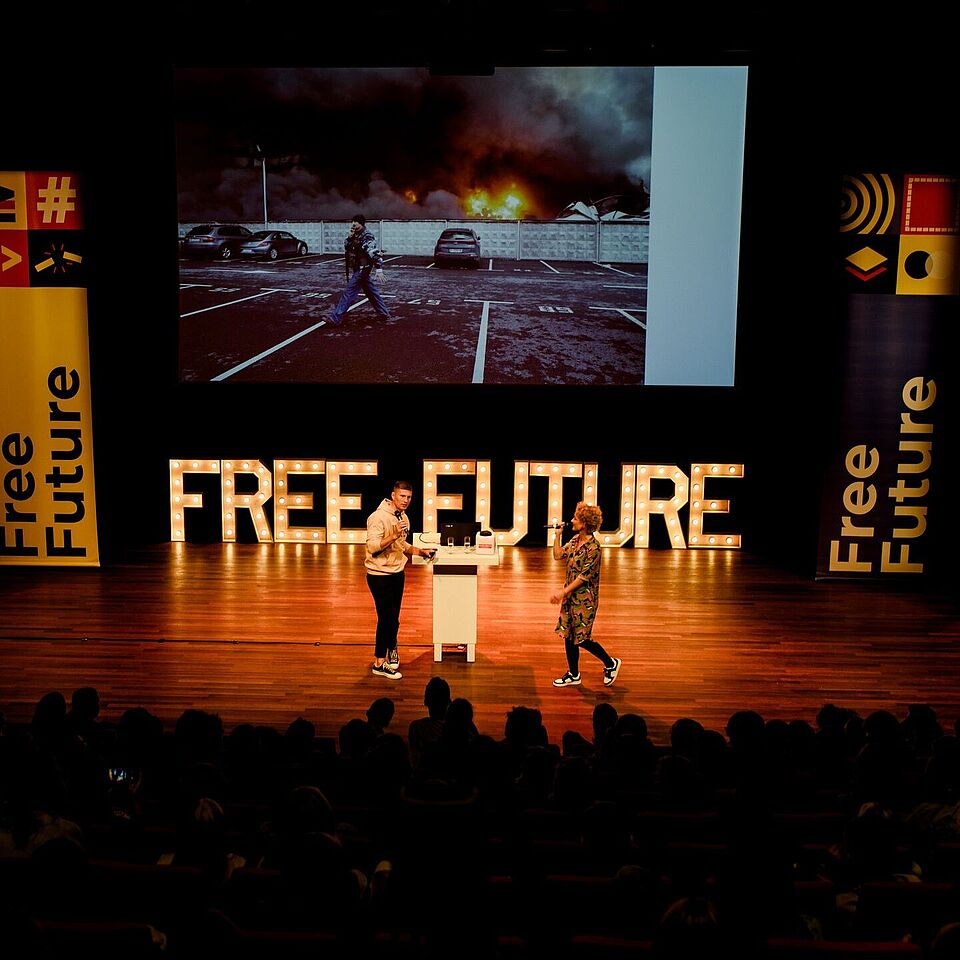 Twee personen staan op een podium. Op de achtergrond is te lezen: Free Future