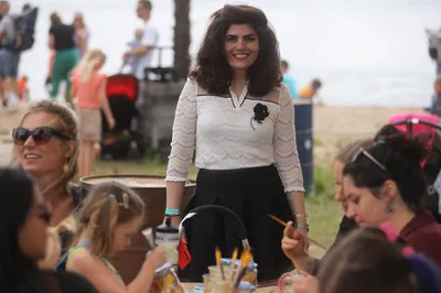 Vrouw glimlacht bij een knutseltafel waar kinderen creatief bezig zijn.