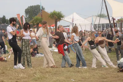 Groep jongeren danst hand in hand op een buitenfestival.