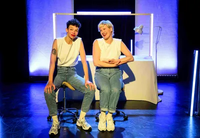 Twee personen in het wit gekleed kijken met een glimlach de zaal in.