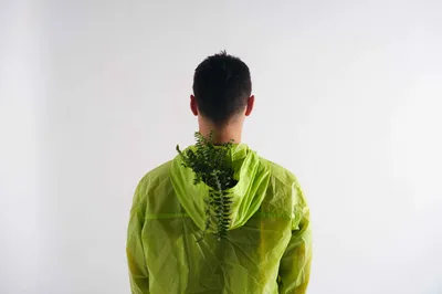 A man is seen from behind, with a small flower in the hood of his green hoodie.