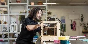 Een man met krullen maakt een object met de 3d printer
