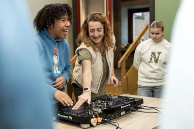 Een leerling en een docent genieten samen terwijl ze DJ-apparatuur uitproberen