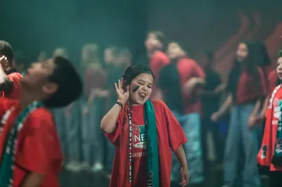 Kind danst vrolijk in rood-groen-zwarte supportersstijl tijdens een podiumoptreden