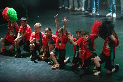 Groep kinderen in rood-groen-zwarte supportersshirts poseert juichend op het podium