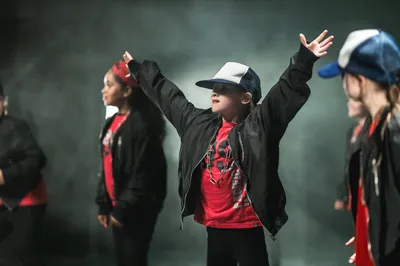 Een kind danst zelfverzekerd op het podium, omringd door energieke mededansers