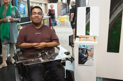 Een jongen in een rolstoel toont trots zijn kunstwerk tijdens een expositie