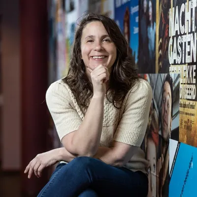 Vrouw poseert lachend voor een kleurrijke muur vol posters.