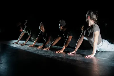 Dansers liggen in een rij op de vloer en duwen zich omhoog in een stretchhouding.