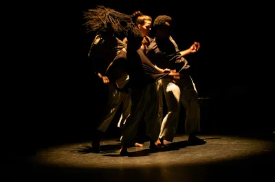 Dansers vormen een compacte groep in een donkere, intense scène.