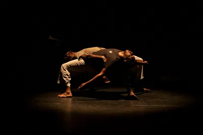 Twee dansers liggen kruisvormig over elkaar in een spotlight.