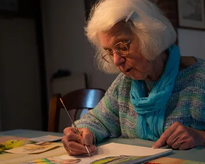 Een vrouw die aan het schilderen is met grijs haar en een bril