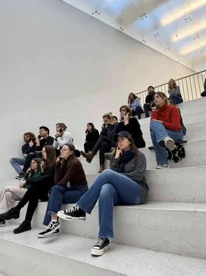 Verschillende studenten zitten op een trap, luisterend naar een kastje die ze voor hun oor houden. 