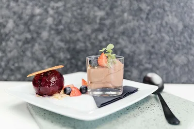 Een wit bord met een glaasje met chocolade mousse en een bolletje rood ijs met vruchtjes ernaast