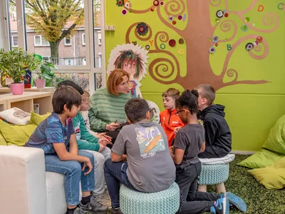 Kinderen zitten om een volwassene heen om te luisteren naar een verhaal