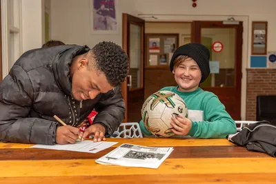 Een profvoetballer zet een handtekening terwijl een kind blij met zijn voetbal toekijkt