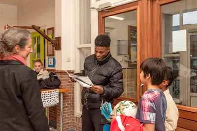 Een groep leerlingen verwelkomt een profvoetballer en bladert nieuwsgierig door een krant