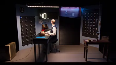 Een man zit aan een bureau en kijkt naar een groot digitaal scherm met het getal veertig dat oplicht in witte cijfers.