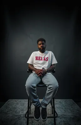 Man zit op een kruk in een donkere studio en kijkt rustig in de camera.