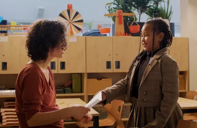 Kind in een klaslokaal geeft een papier aan een volwassene terwijl ze samen glimlachen