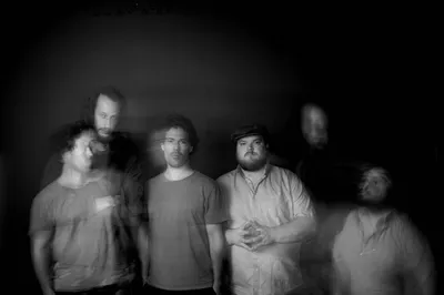 De drie mannen van de band kijken in de camera, door een effect is hun beweging nog wazig langs hen heen te zien.