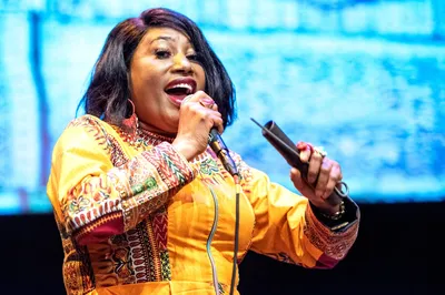 Een vrouw in een kleurrijke outfit zingt in een microfoon en kijkt energiek het publiek in