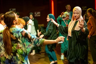 Een groep vrouwen danst samen in een warme, feestelijke sfeer. Ze staan met uitgestrekte armen op de dansvloer, omringd door anderen die meebewegen en genieten van het moment