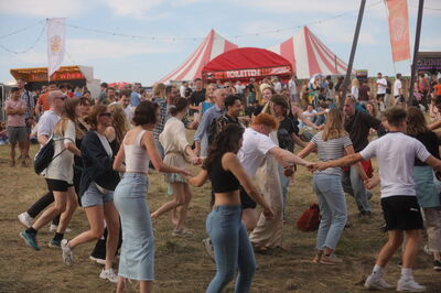 Dansende festivalgroep in een grote cirkel op het grasveld.
