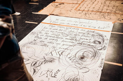 Grote vellen papier op de vloer met handgeschreven teksten en expressieve krullen en tekeningen