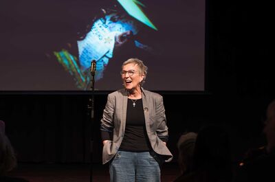 Een vrouw staat op het podium en kijkt lachend het publiek in.