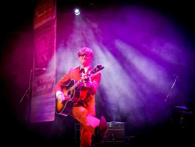 Een man danst spelend op zijn gitaar over het podium.
