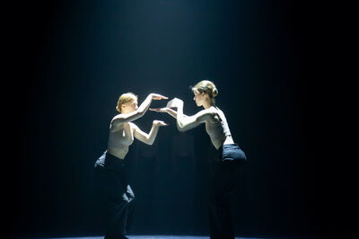 Twee danseressen staan in een danspose naar elkaar toe gericht. Boven hen een blauwe spot. 
