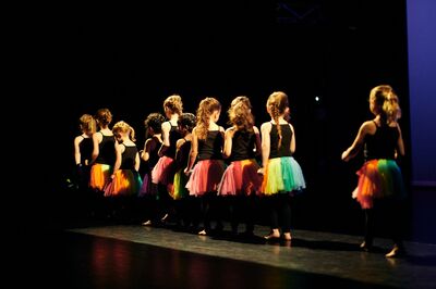 Kinderen in kleurrijke rokjes dansen samen op een podium.