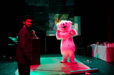 Acteur in ijsberenpak met bord “Save the Planet” op een toneel, met projectie en andere spelers op de achtergrond.