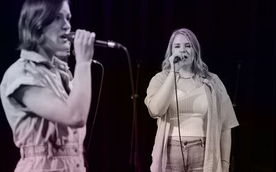 Twee vrouwen staan haaks op elkaar voor zich uit te zingen. 