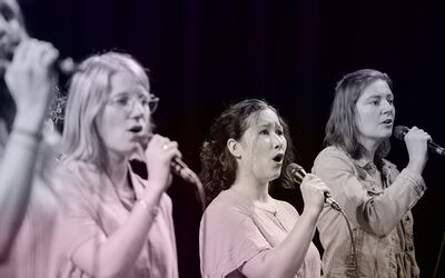 Een zoom in op vier vrouwen die met een microfoon geconcentreerd aan het zingen zijn. 