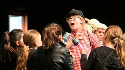 Een meisje met een petje en een rood geruit blouseje zingt.