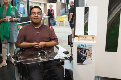 Een jongen in een rolstoel toont trots zijn kunstwerk tijdens een expositie