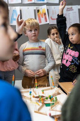 Kinderen werken geconcentreerd aan een maquette met kralen en stokjes in de klas