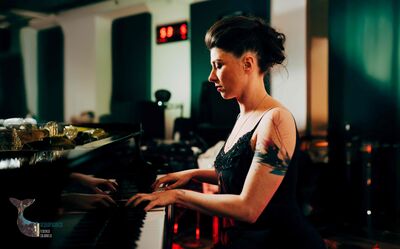 We zien een elegant geklede vrouw gefocust piano spelen.