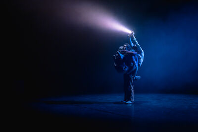 Drie mannen houden elkaar op een acrobatische beweging vast en schijnen met een lamp in de verte.