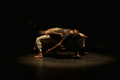 Twee dansers liggen kruisvormig over elkaar in een spotlight.