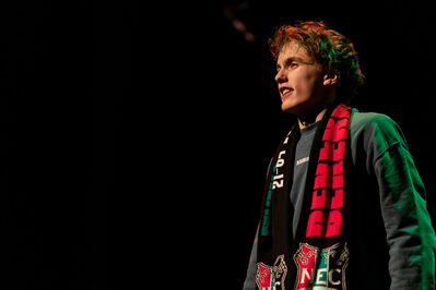 Jongere op een donker podium met club-sjaal in rood, groen en zwart