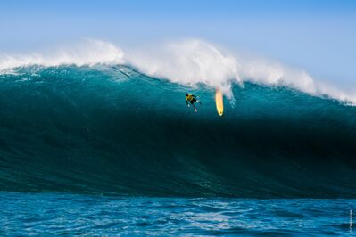 Surfer valt van een grote, krachtige golf terwijl zijn surfboard naast hem drijft.