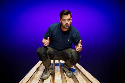 Jasper van der Veen hurkt op een houten podium en kijkt geconcentreerd voor zich uit, met een paars-blauwe theaterachtergrond.