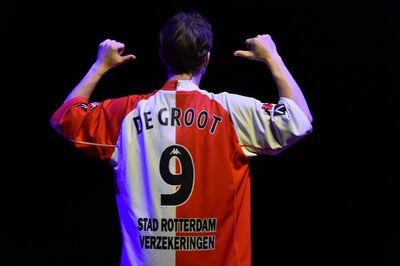 Rory staat omgedraaid en wijst met zijn duimen naar zijn rugnummer op zijn voetbalshirt.