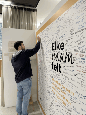 Een jongen van midden 20 schrijft een naam op de muur met honderd andere namen.